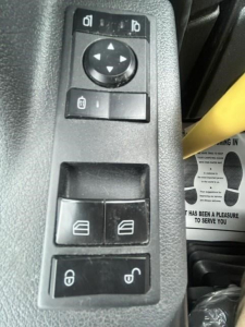 Truck interior switch panel with window controls and mirror adjustment dial in a Freightliner Cascadia cab interior.
