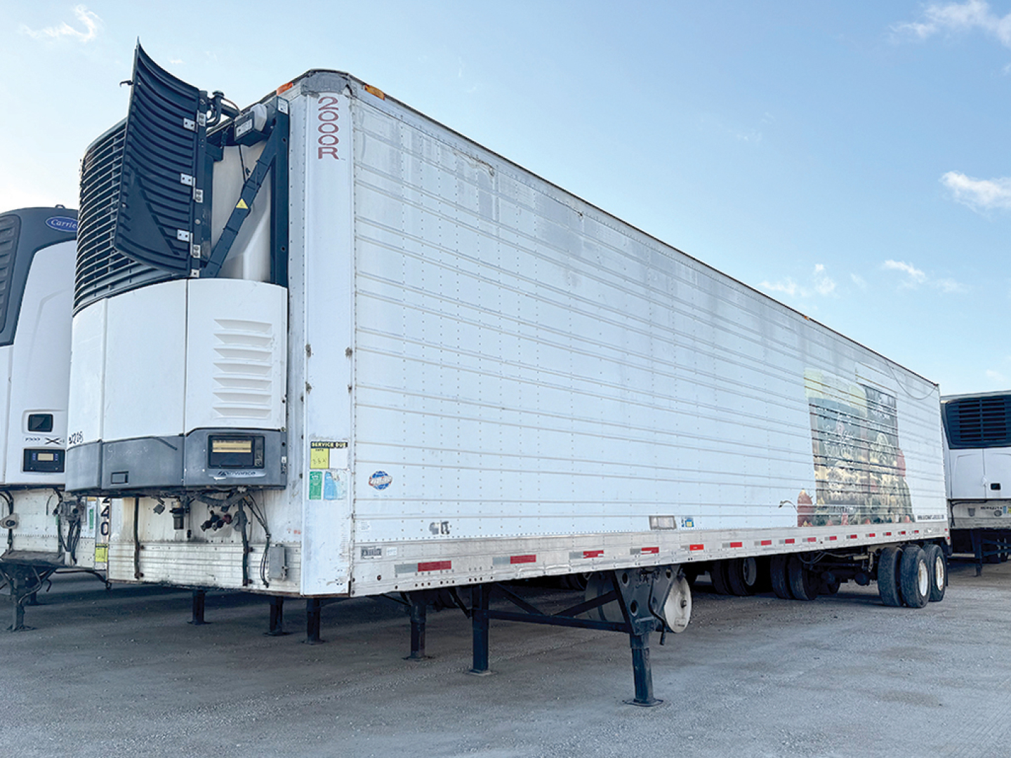 Utility 2000R refrigerated trailer in side view showing reefer unit and corrugated side panels with VIN sticker and stock number visible.