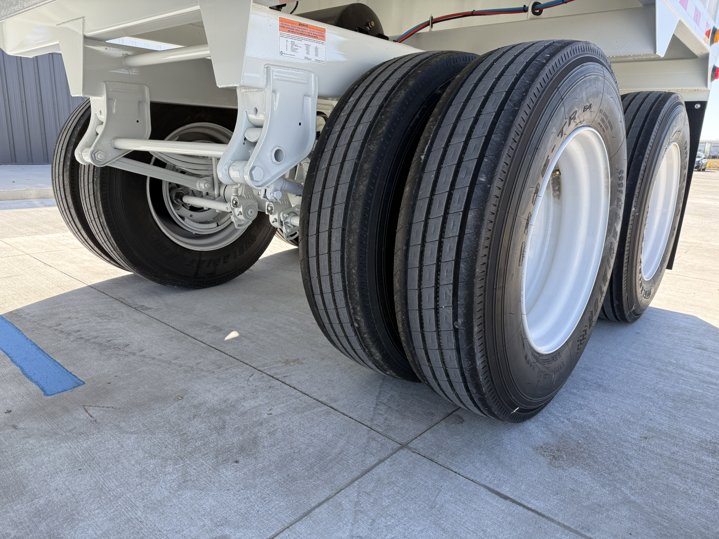 Heavy-duty trailer axle with dual tires and white frame visible; close-up of rear wheels and suspension of a 2027 Armor Lite 40' steel grain hopper.