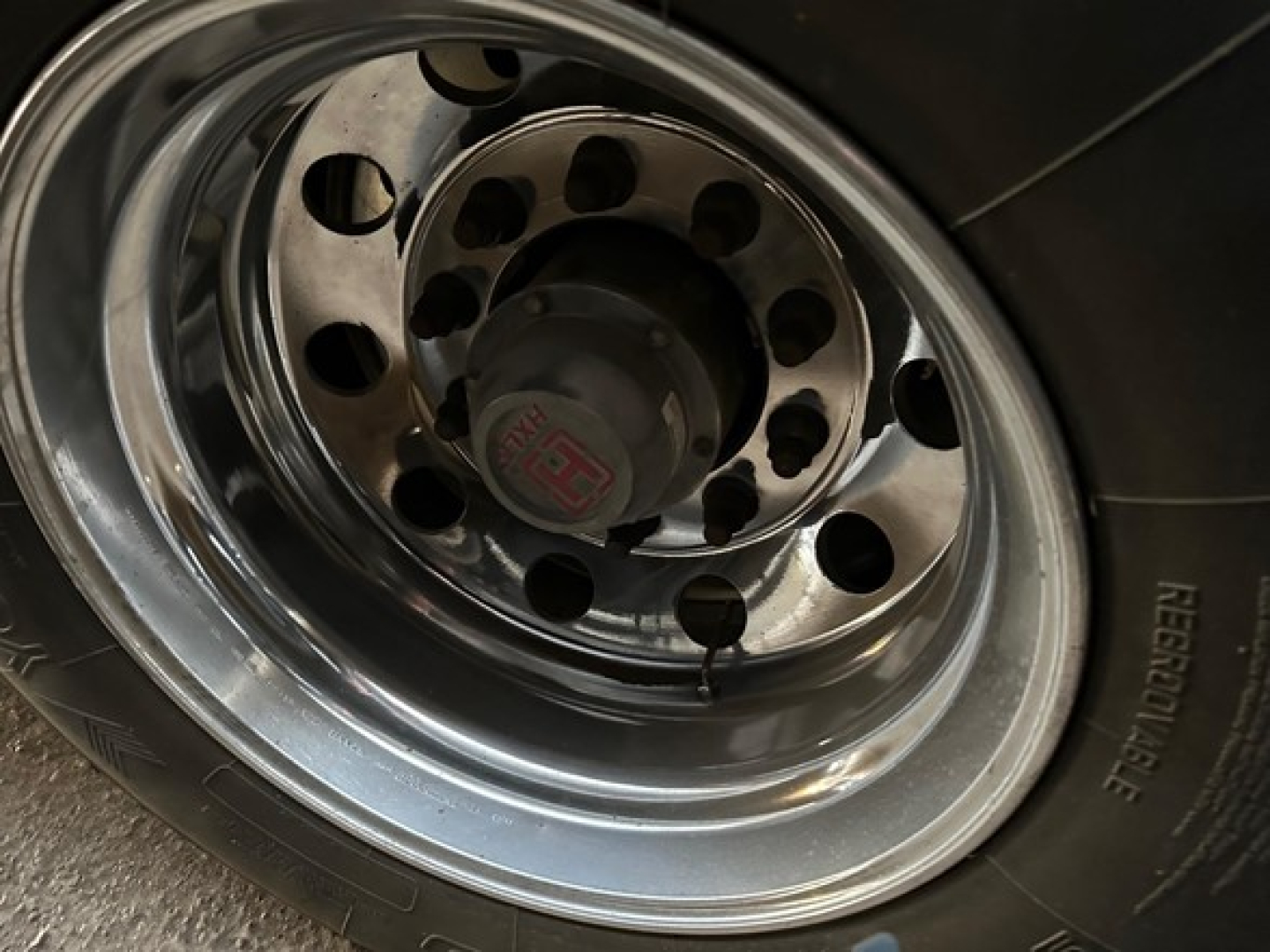 Wheel and tire close-up on a MacAll aluminum Conestoga sliding tarp trailer wheel hub and polished rim with lug holes visible