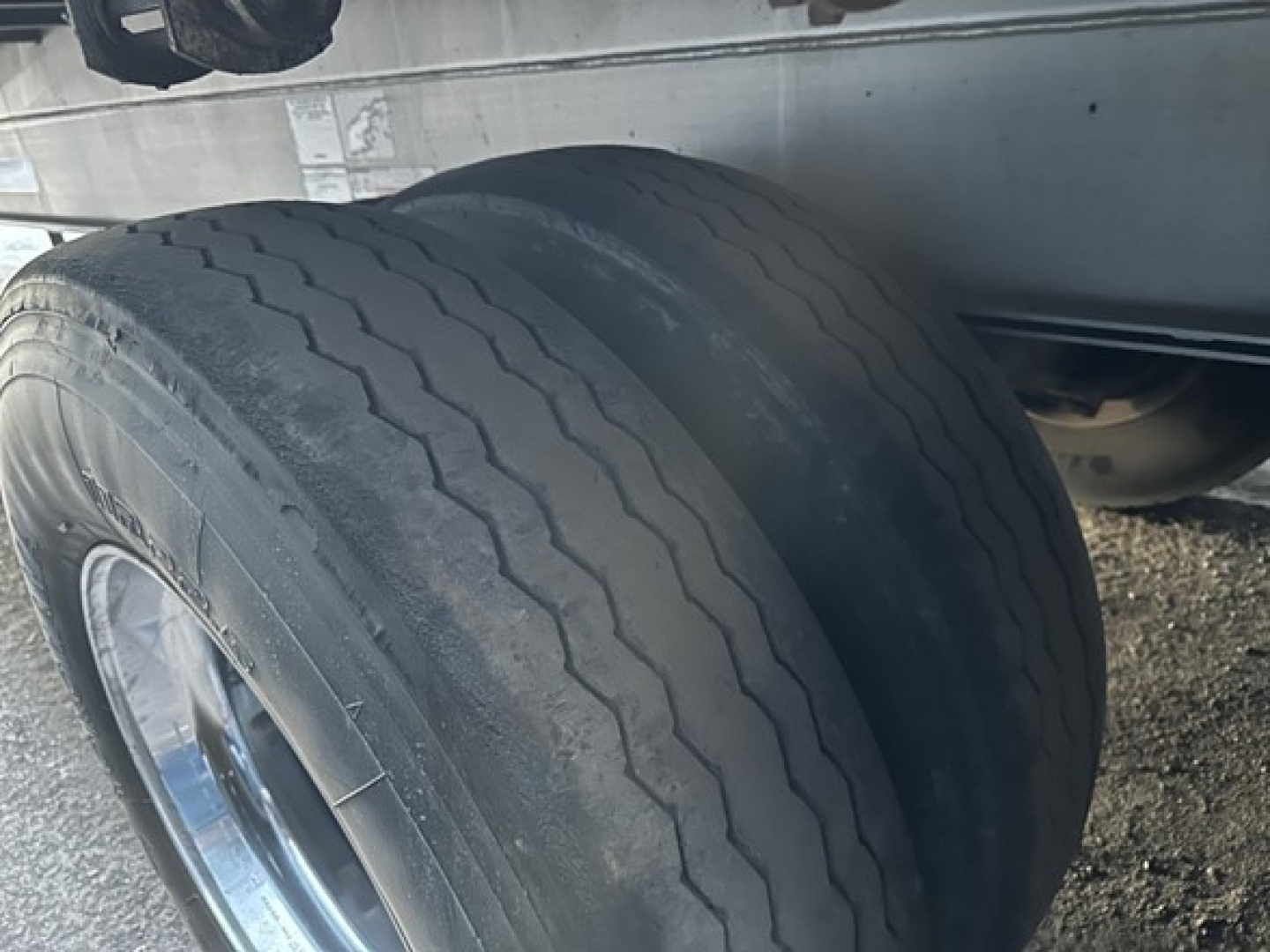 Trailer tire view with tread pattern and chrome wheel, undercarriage visible; part of Conestoga sliding tarp system trailer.