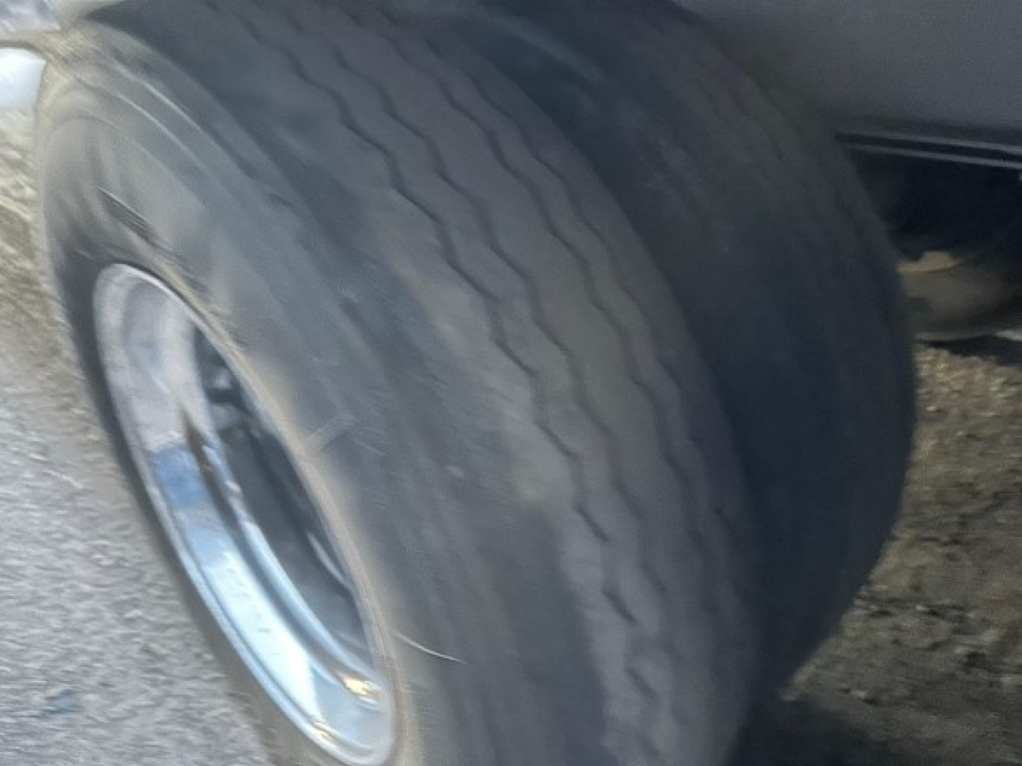 Trailer wheel and tire view of a Mac all-aluminum Conestoga sliding tarp system showing tire treads and wheel hub.