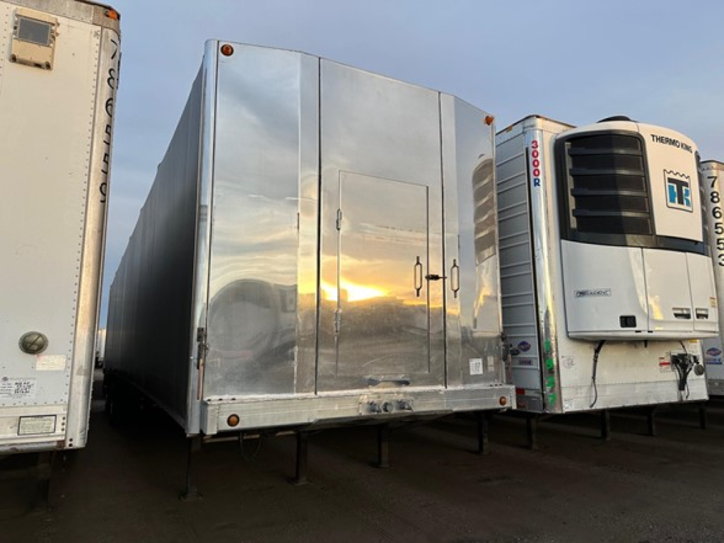 Trailer showing a 2023 Mac All Aluminum Conestoga sliding tarp system in a curtainside trailer setup with reflective aluminum sides and a front access door.