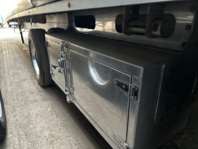 Trailer underside showing a metal storage box mounted under a Mac All Aluminum W Conestoga sliding tarp system, with wheel and suspension components visible.