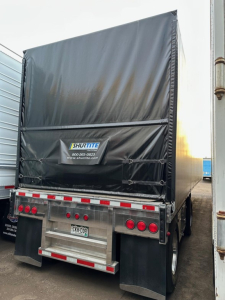 Trailer rear view showing 2023 Mac aluminum Conestoga sliding tarp system with Shurtle banner, black tarp, rear lights, and mud flaps.