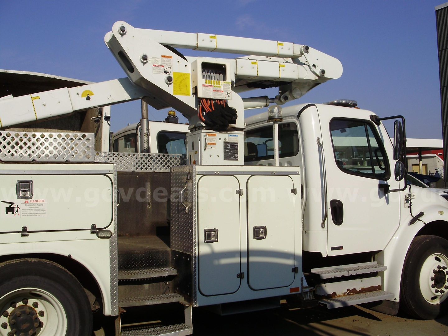 Truck side view showing bucket lift and work compartments on Freightliner M2 106 utility body with white cab and bucket platform.