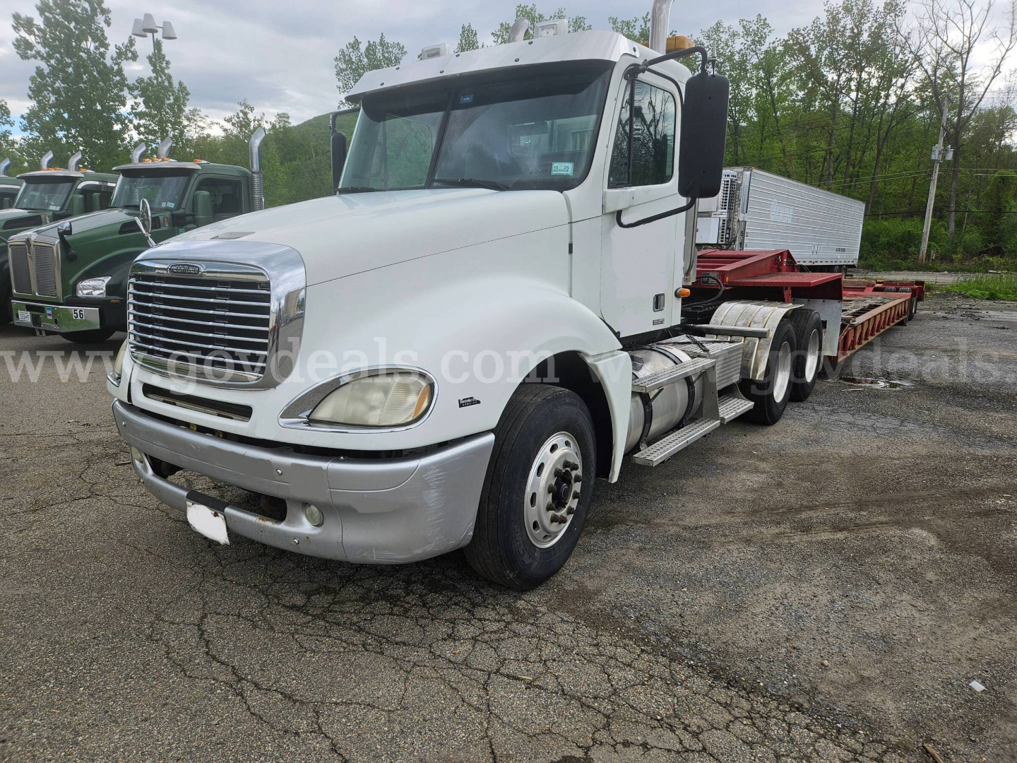 Truck cab of a 2003 Freightliner Columbia 120 with a flatbed trailer in a lot, white cab, chrome grille, dual rear axles, VIN 1FUJA6CV33LL79728.