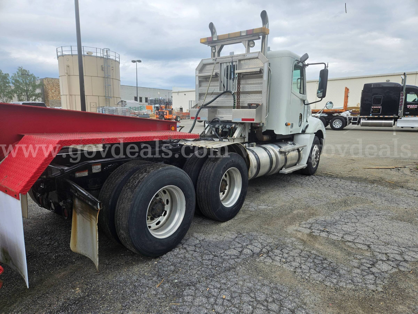 Truck rear-side view of a 2003 Freightliner Columbia 120 tractor with red flatbed trailer, showing dual rear axles and exhaust stack.