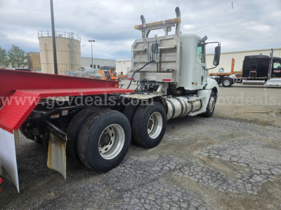 Truck rear-side view of a 2003 Freightliner Columbia 120 tractor with red flatbed trailer, showing dual rear axles and exhaust stack.