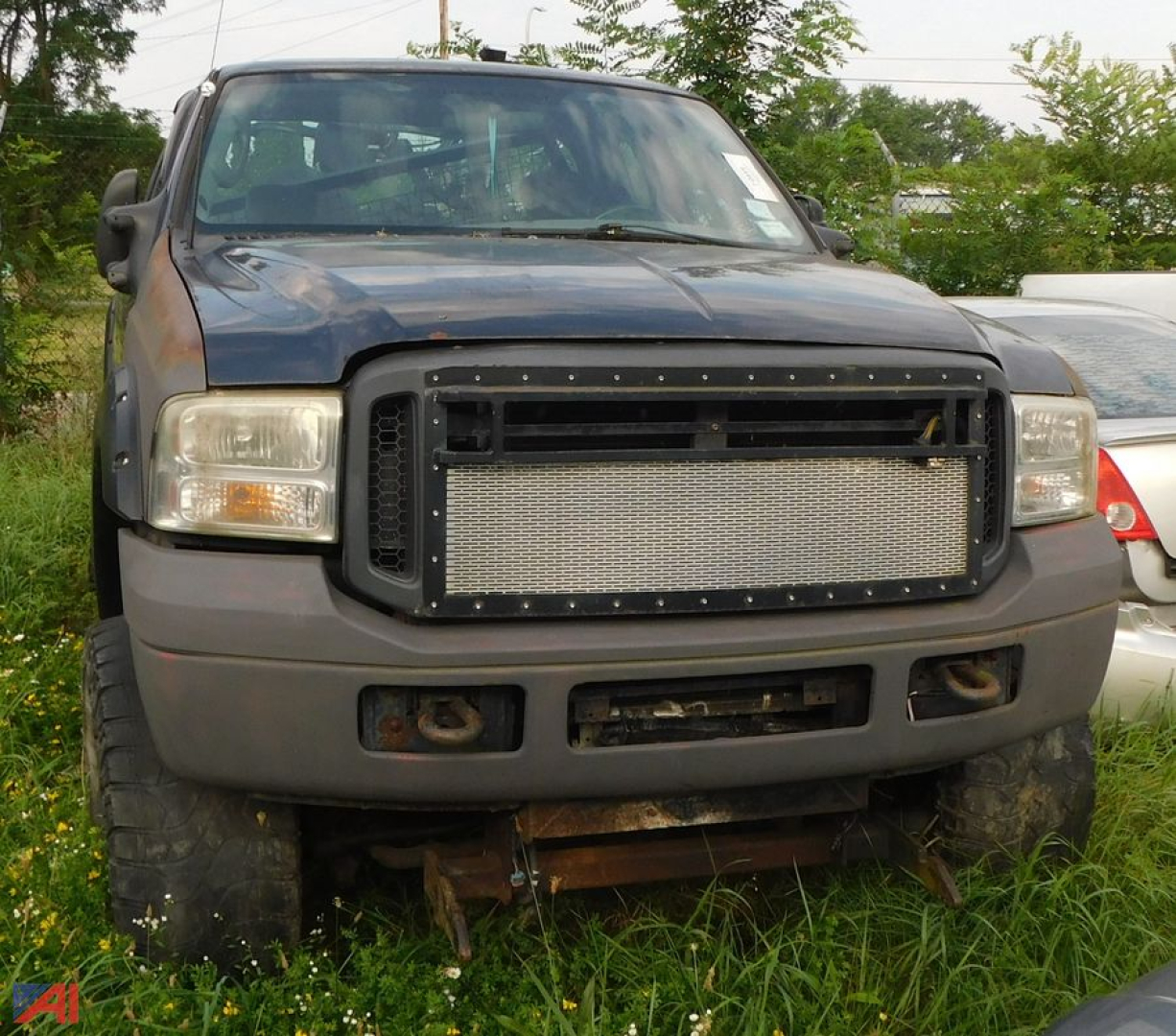 Front view of a blue 2003 Ford F-350 Super Duty pickup with a large aftermarket grille and plow mount, extended cab, 4x4, in grassy lot.