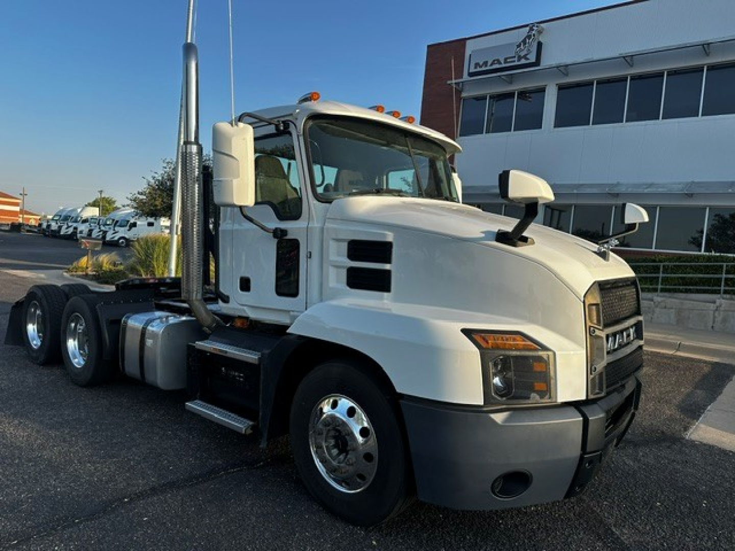 Truck cab showing 2021 Mack Anthem conventional daycab with white exterior, dual rear axles, large side mirrors, and Mack dealership in background; VIN and stock number not visible in text on image.