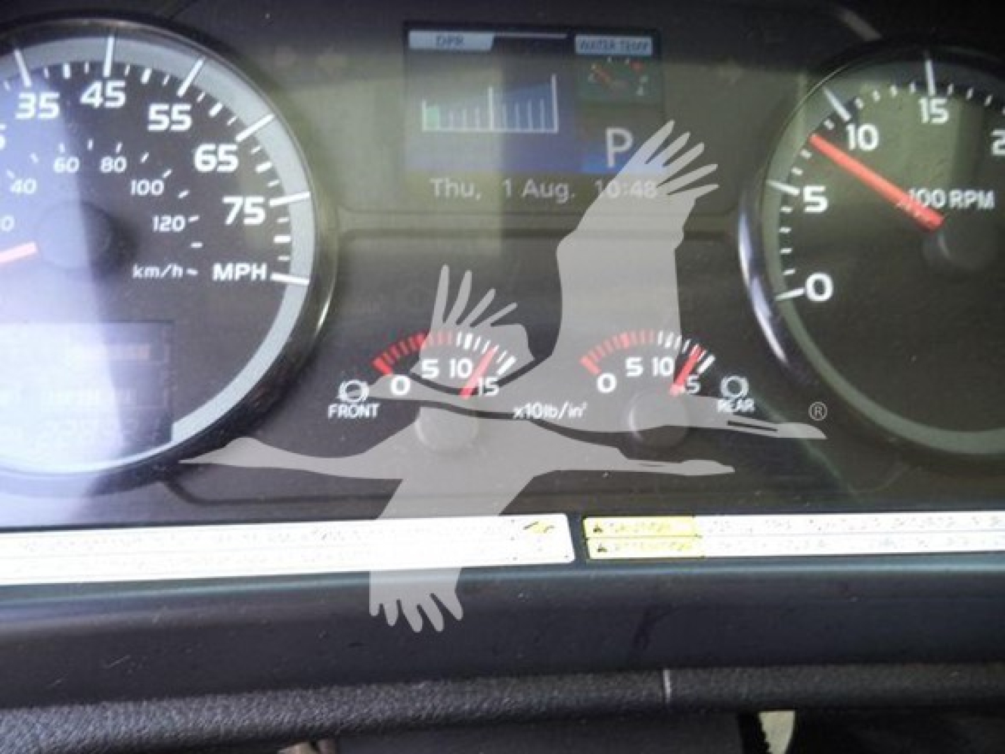 Dashboard of a Hino truck showing gauge clusters with speedometer and RPM, center display with date, and warning dials. Visible text includes MPH/KPH scales, dials, and a reflection of hands on the screen.
