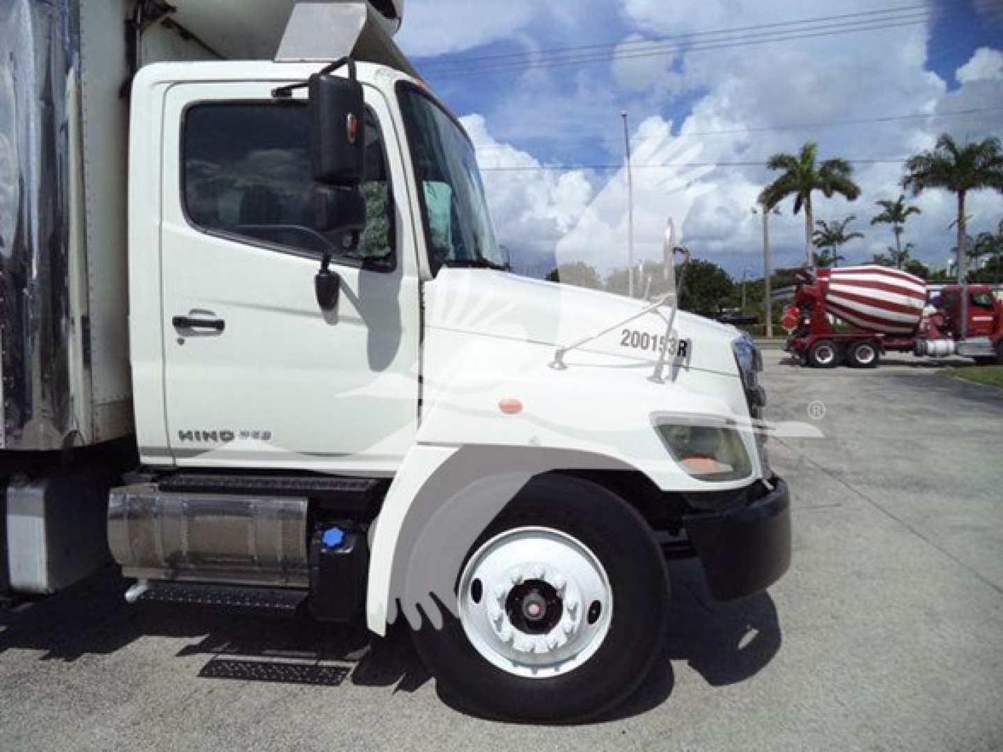 Hino 268A refrigerated truck cab side view showing front wheel and door with Hino badge. Visible text includes '2001S?' on fender and chrome fuel tank; background shows palm trees and other trucks.