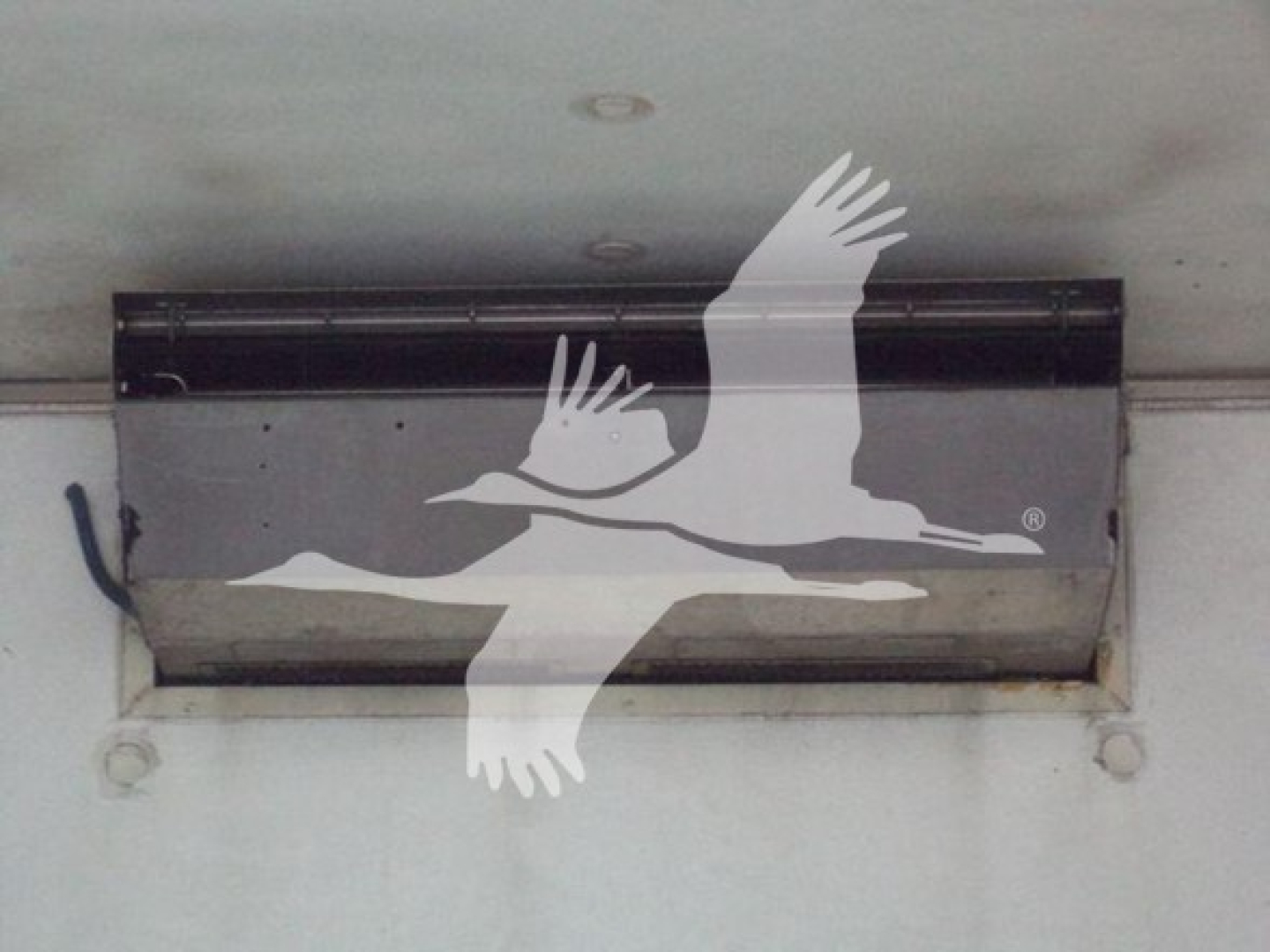 Refrigerated truck cargo area vent with a black metal vent hatch mounted to a white trailer wall.