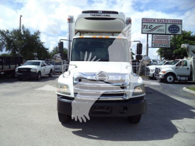Front view of a Hino refrigerated truck with Thermo King unit on cab, visible signage in background, front grille and headlights.