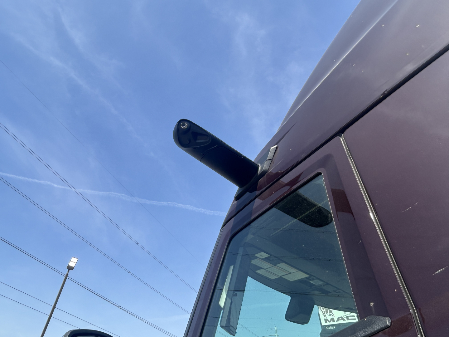 Truck side mirror and window of a new Mack PR64T76H sleeper cab with a clear blue sky