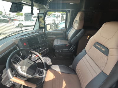 Interior of a new Mack PR64T76H truck cab showing steering wheel, dashboard, and two-tone seats with Mack logo on the passenger seat.