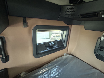 Interior of truck cab showing tan side panel with a small window, overhead console, and part of a sleeper area.
