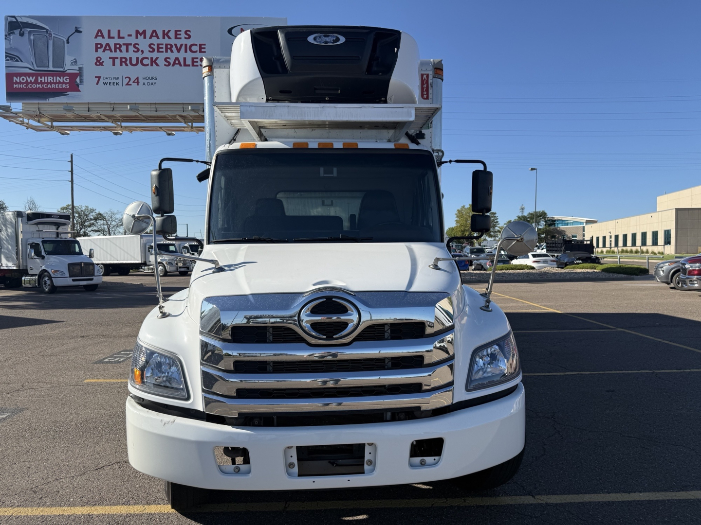 Front view of a 2021 Hino 338 refrigerated truck with a raised refrigeration unit on the cab roof, chrome grille, and dual side mirrors.