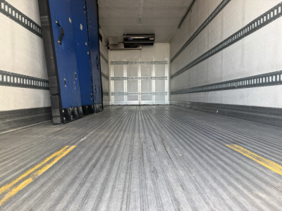 Interior of a refrigerated box truck trailer showing ribbed floor, sidewall tracks, and a blue mechanical unit near the left wall.