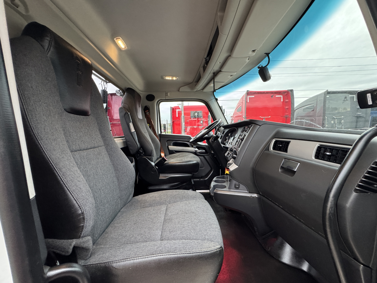 Truck cab interior showing the driver and passenger seats, dashboard, steering wheel, and overhead lights.