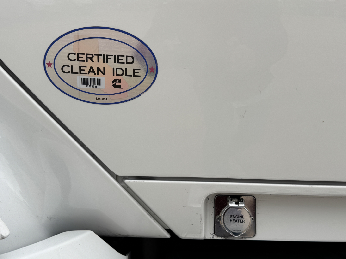 Kenworth T680 engine bay area showing Certified Clean Idle badge and engine heater plug cover on rear side panel.