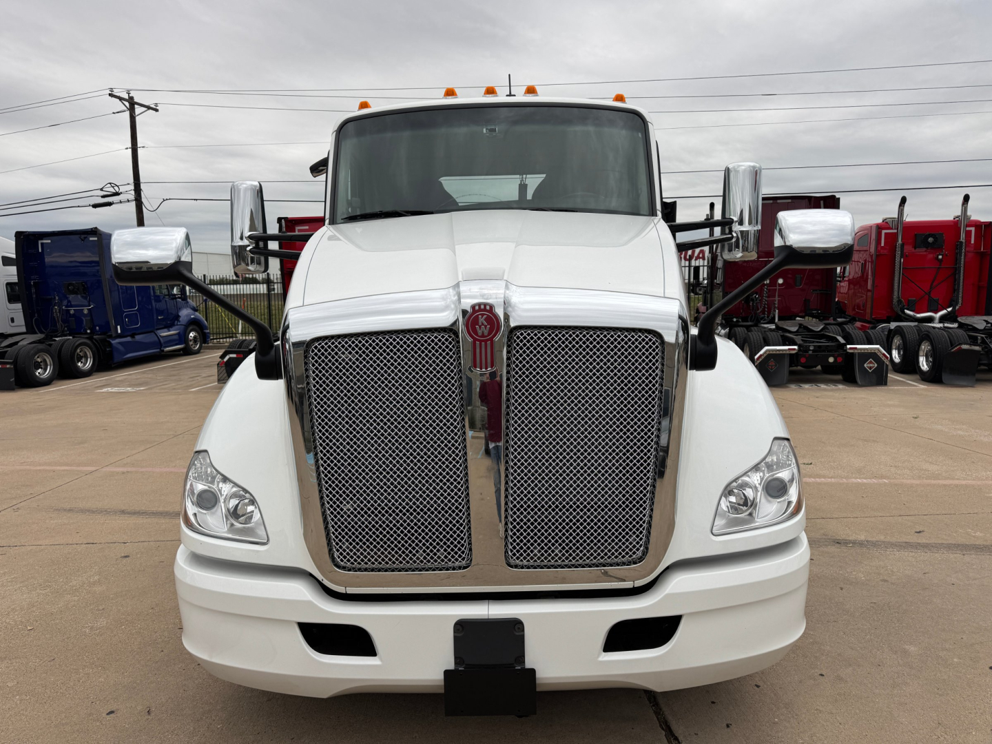 Kenworth T680 front view showing large chrome grille and bumper, white cab, emblem in center grille, side mirrors, and running lights.