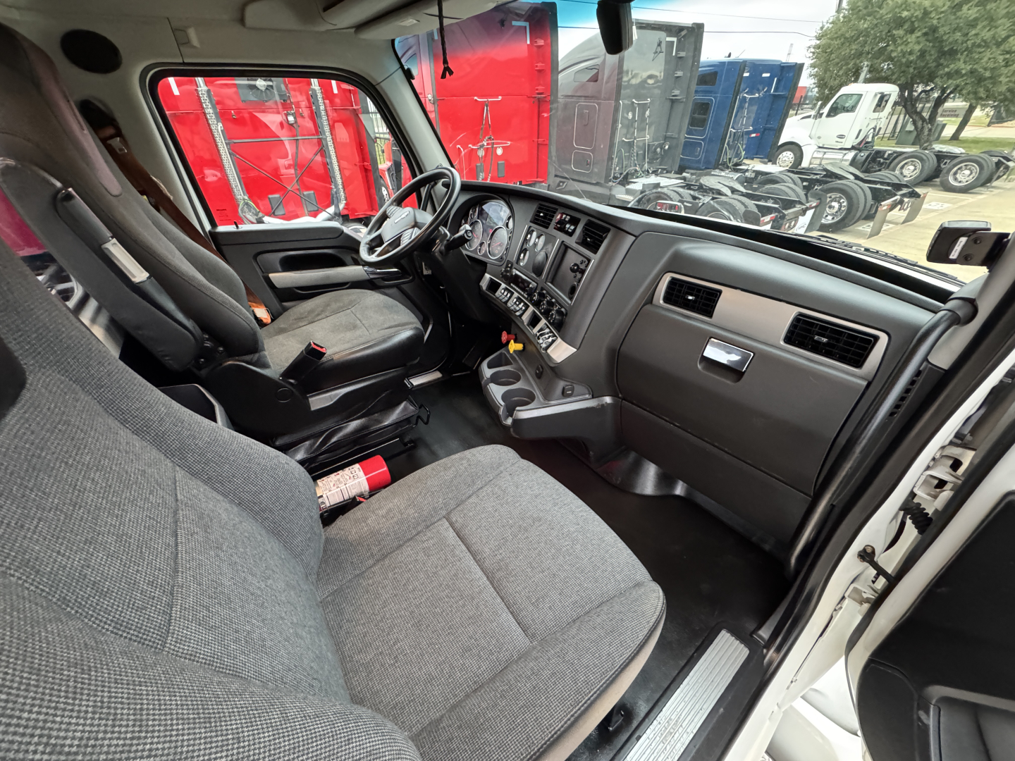 Truck cab interior of a 2022 Kenworth T680 showing driver seat, steering wheel, dashboard, and center console with controls.