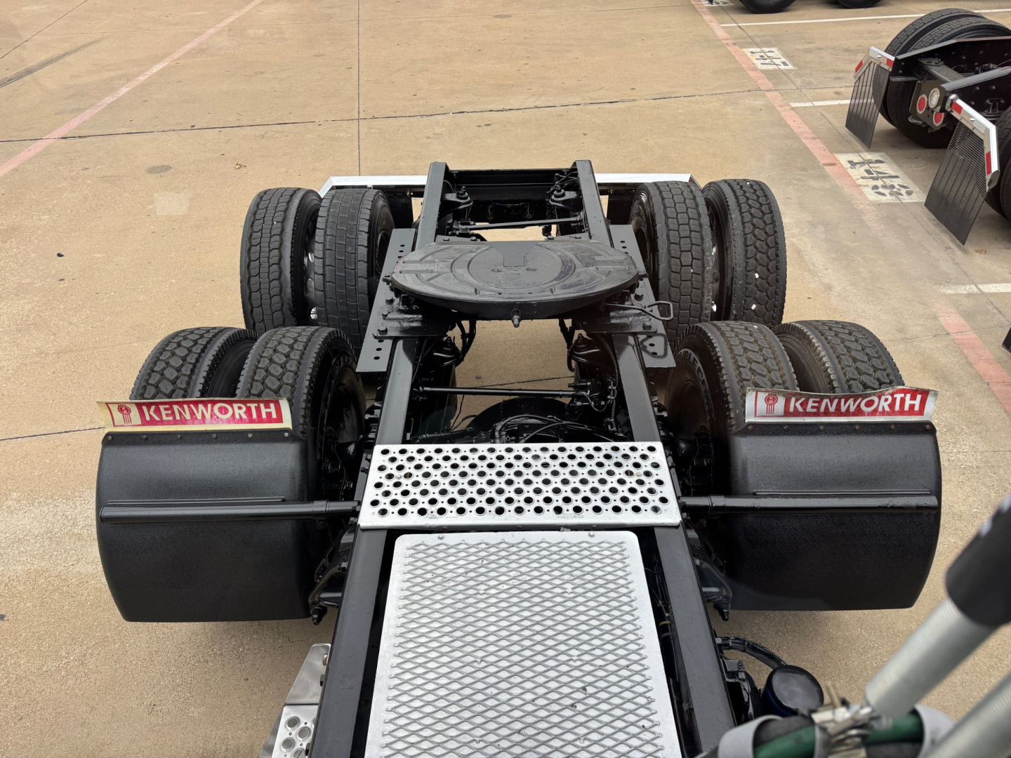 Kenworth 2022 T680 tractor chassis and fifth wheel area showing rear view, dual rear axles, Kenworth mud flaps, and aluminum diamond plate platform.