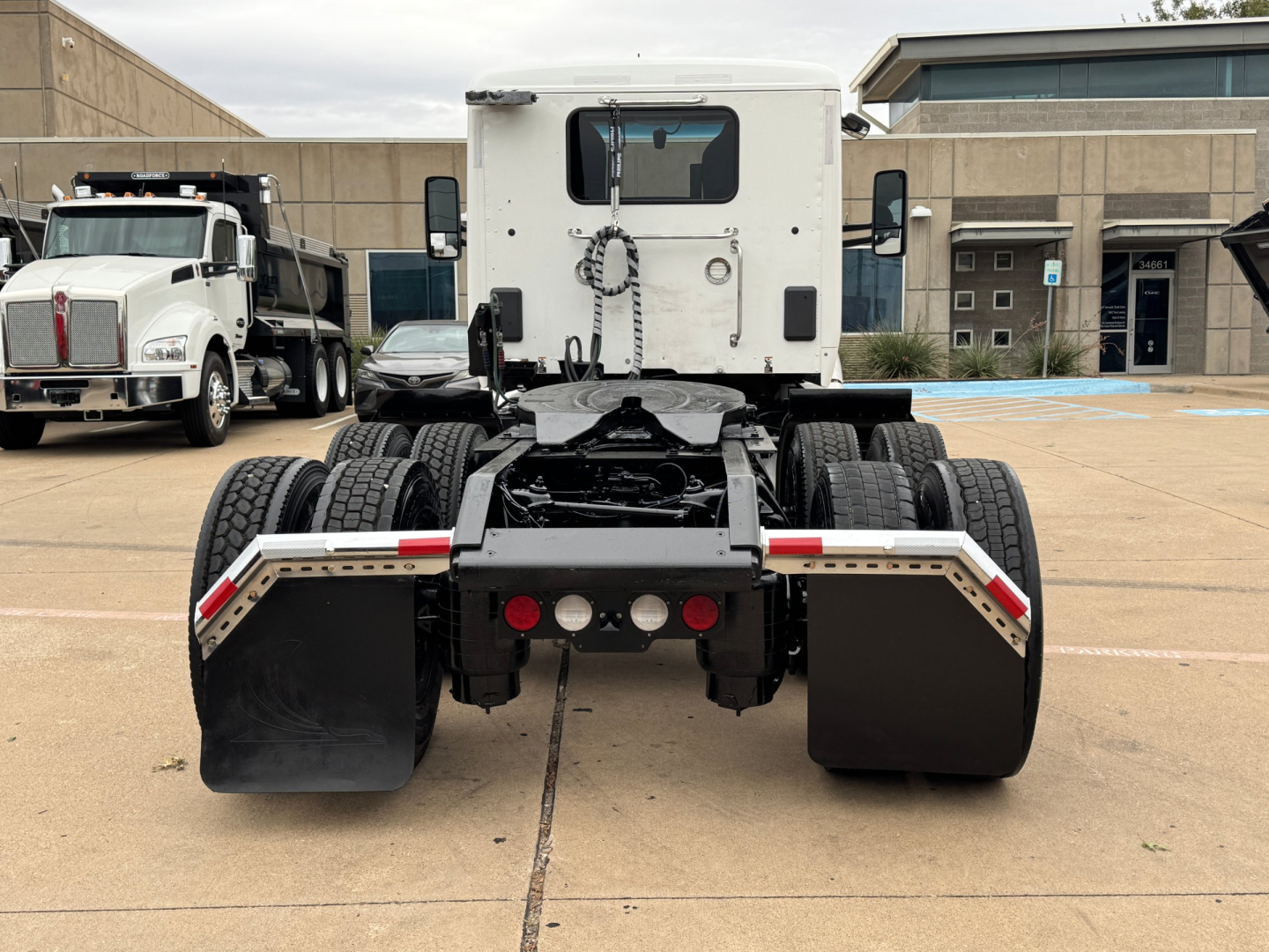 Semi truck rear view showing fifth wheel, suspension, and dual rear axles of a Kenworth T680 with white cab in a truck lot.