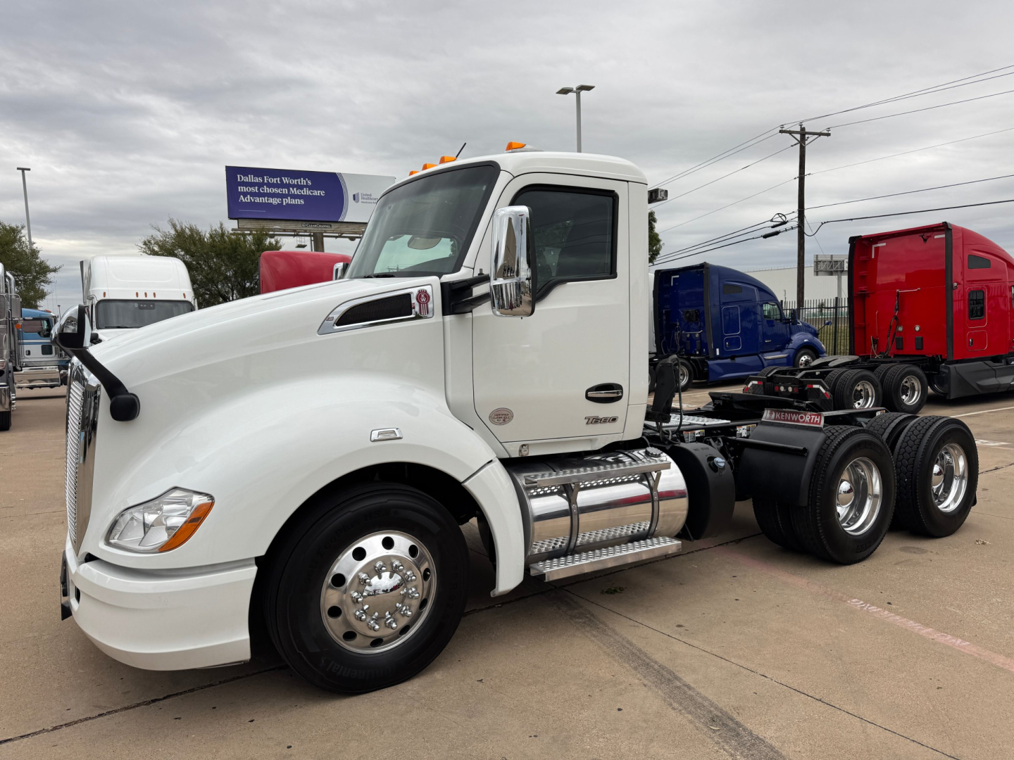 Kenworth T680 truck with white cab, side view showing chrome fuel tanks, steps, and dual rear axles. Visible text on cab includes Kenworth badge and exhaust.