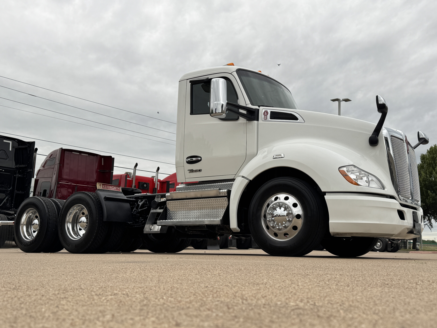 Kenworth T680 conventional daycab truck in off-white with chrome fuel tanks and dual rear axles, side view showing VIN and stock info sticker