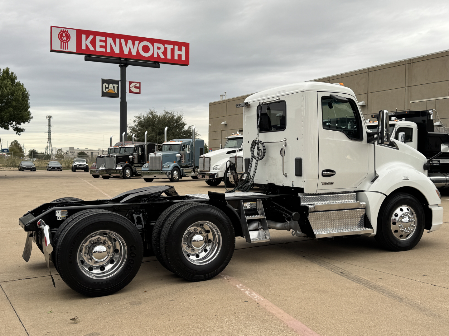 Kenworth T680 truck in a dealership lot with white cab and black chassis, dual rear axles and chrome steps.