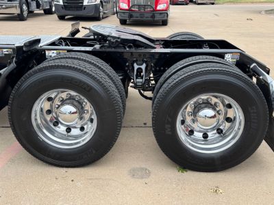 Kenworth T680 wheel area showing dual rear axles with chrome wheels and bold tires, chassis frame, and suspension components visible.