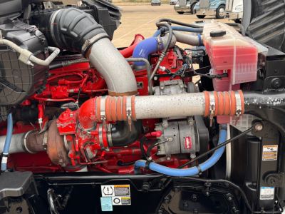 Kenworth T680 engine bay showing red engine components, blue hoses, intake piping, coolant reservoir, and turbocharger.