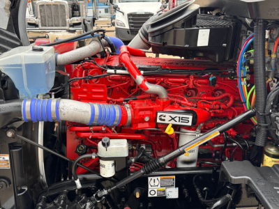 Kenworth T680 engine bay showing XD15 diesel engine with red painted block, blue intake hose, coolant reservoir, and various hoses and components.