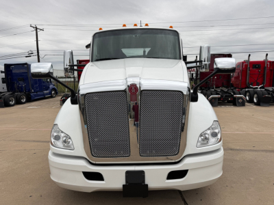 Kenworth T680 front view showing large chrome grille and bumper, white cab, emblem in center grille, side mirrors, and running lights.