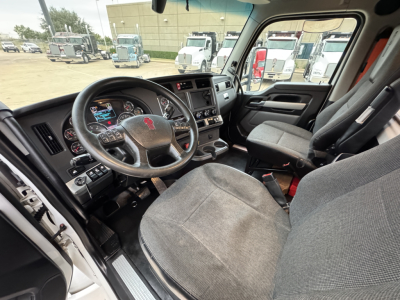 Kenworth T680 truck interior showing steering wheel with logo, dashboard, and driver seat; front passenger seat and center console visible.