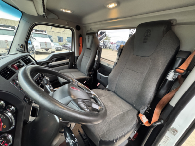 Cab interior of a 2022 Kenworth T680 daycab showing steering wheel, driver's seat, and passenger seat with seat belts visible.
