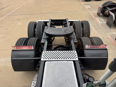 Kenworth 2022 T680 tractor chassis and fifth wheel area showing rear view, dual rear axles, Kenworth mud flaps, and aluminum diamond plate platform.