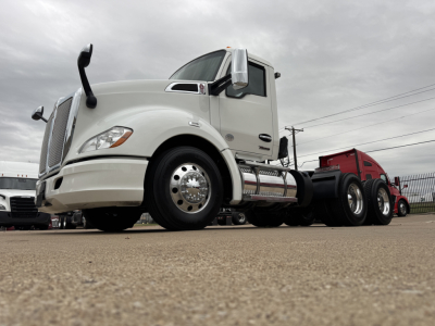 Kenworth T680 tractor cab with white exterior, side fuel tanks, chrome exhaust, and dual rear axles visible; large front grille and headlight assembly.