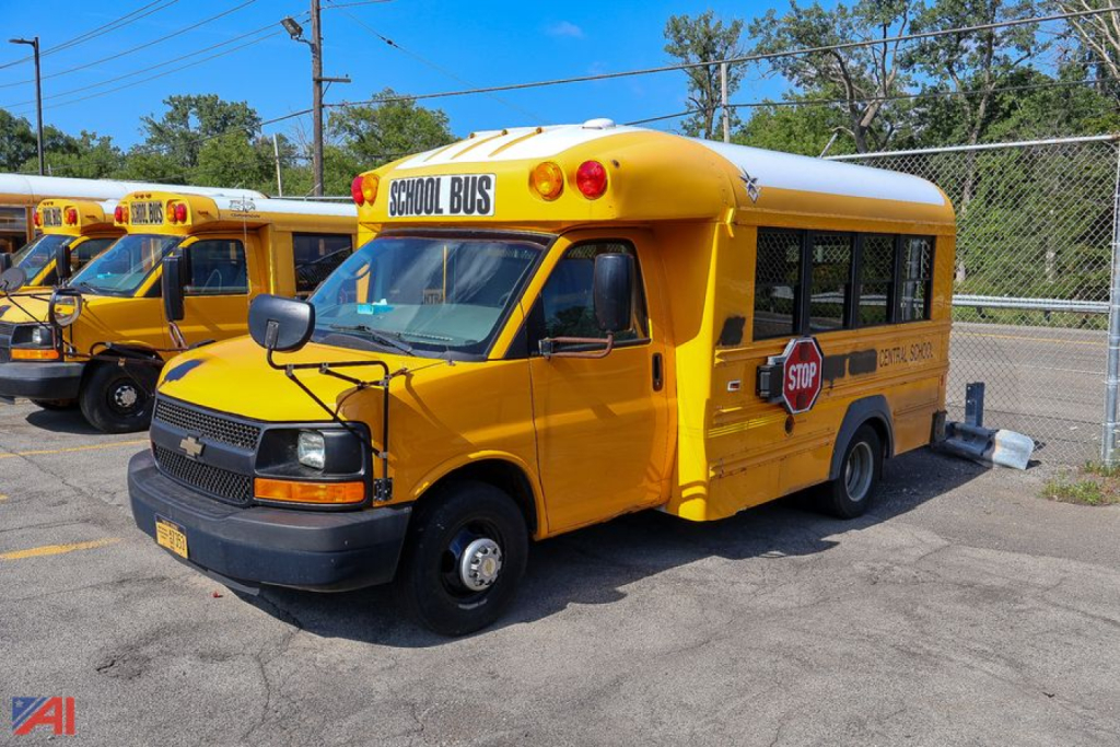 Side view of a yellow 2014 Chevrolet Express/Trans Tech school bus with STOP sign extended and 'SCHOOL BUS' signage on the roof, parked in lot.