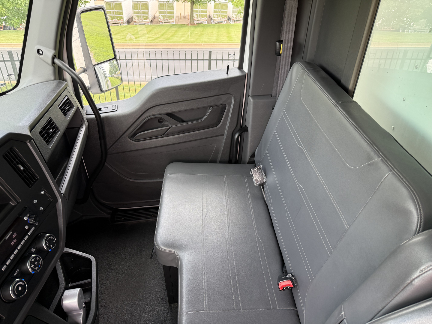 Kenworth T380 cab interior view showing front driver seat and bench passenger seat with grey upholstery, steering wheel, dashboard controls, and door panel.