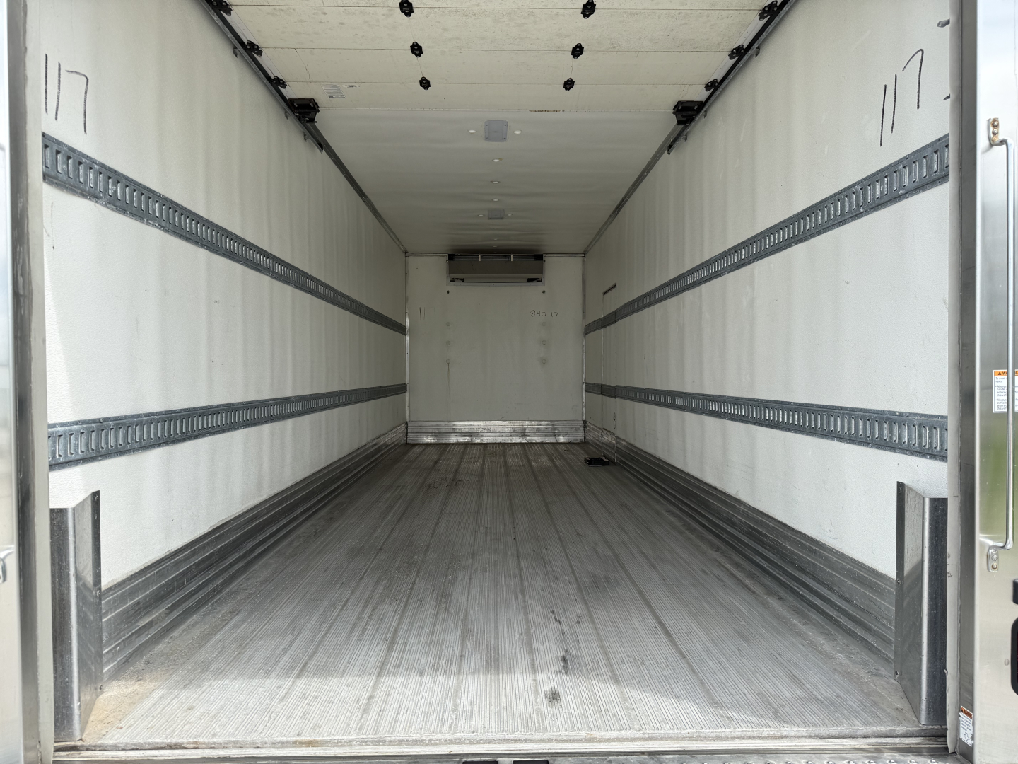 Truck cargo area of a 2023 Kenworth T380 refrigerated truck with empty aluminum cargo space and interior side rails.