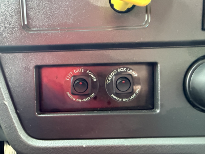 Truck dash panel showing two switches labeled LIFT GATE and CARGO BOX LAMP; circular push buttons with labels around the rims.