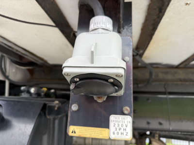 Kenworth T380 undercarriage showing electrical junction box and a yellow warning label, with a 230V 3PH 60Hz unit plate mounted on a dark frame.