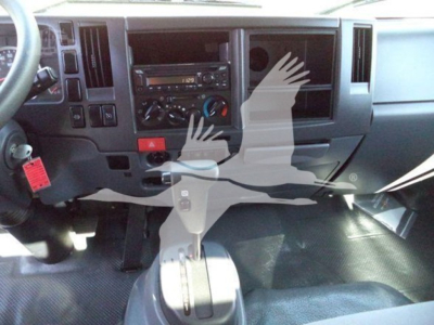 Isuzu truck cab interior showing dashboard with radio, climate controls, gear shifter, and a red hazard button; partial steering wheel and pedals visible.