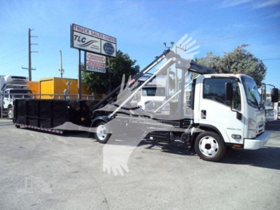 Isuzu NRR roll-off truck with hydraulic arm and dump body, white cab, black dump container, on lot.
