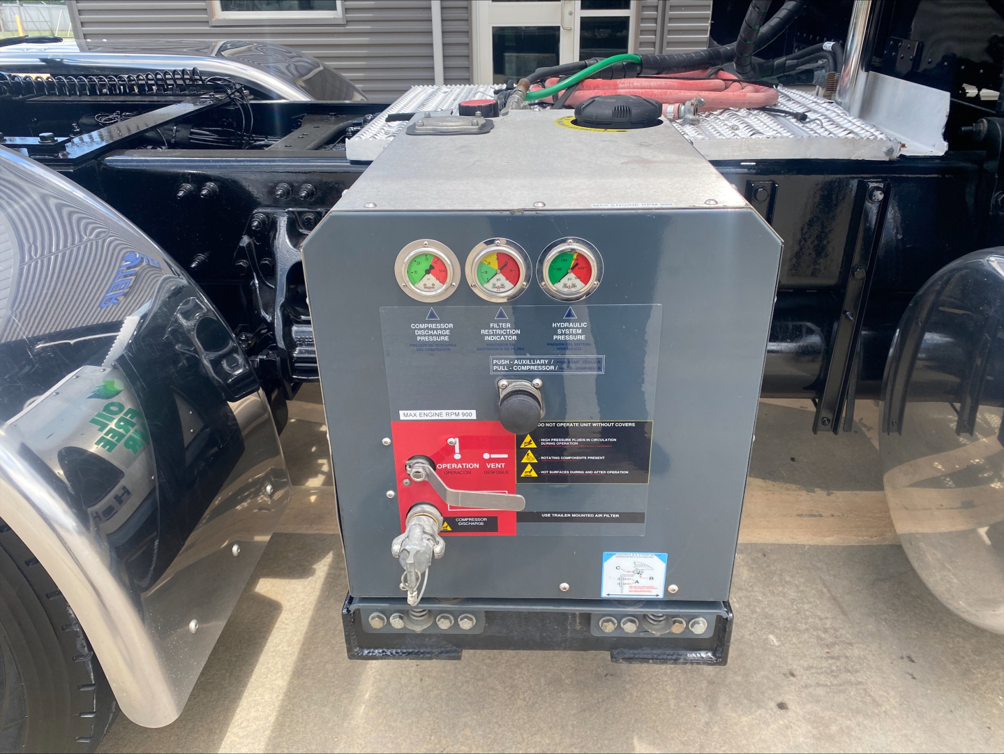Panel mounted control box with three gauges and warning labels on a Peterbilt 389 cab chassis, connected to truck frame; tools and cables visible nearby.