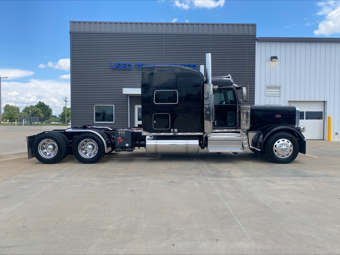 Peterbilt 389 conventional sleeper truck side view showing long hood, black paint, chrome exhaust stacks, and triple rear axles.